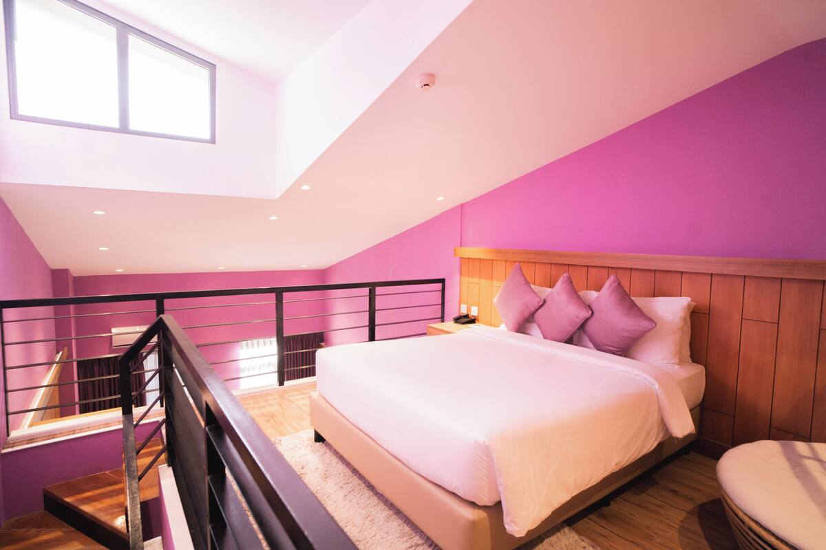 Une chambre à coucher avec un lit, une table de chevet, une fenêtre et un escalier.