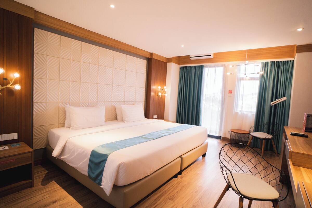 Une chambre d’hôtel avec un grand lit, un bureau, une chaise et une fenêtre avec des rideaux.