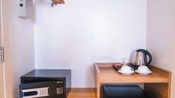A compact kitchenette with a microwave, coffee maker, and a small refrigerator. There is a wooden shelf with a pair of shoes and a hanging garment rack.