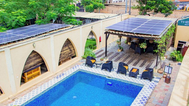 A swimming pool with a tiled deck, solar panels, and outdoor seating. - Villa De l'Intégration (Ouagadougou)