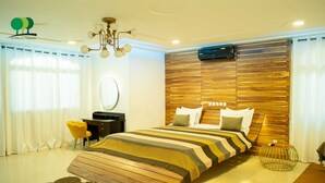 A modern bedroom with a wooden headboard, a striped bedspread, a round mirror, and a yellow chair. - Villa De l'Intégration (Ouagadougou)