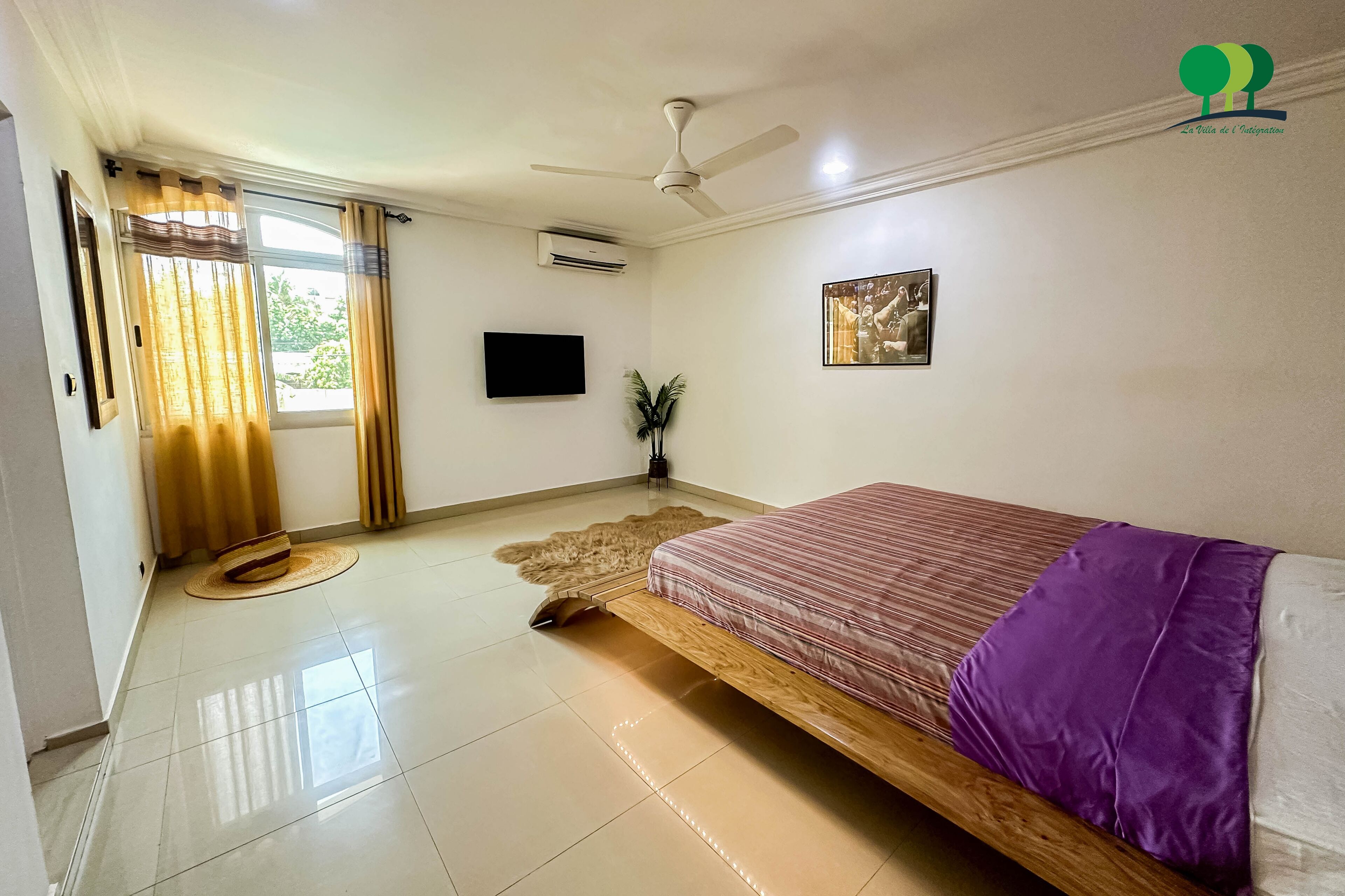 A bedroom with a bed, a ceiling fan, a TV, and a window with curtains.
