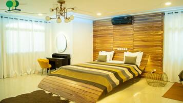 A modern bedroom with a wooden headboard, a striped bedspread, a round mirror, and a yellow chair.