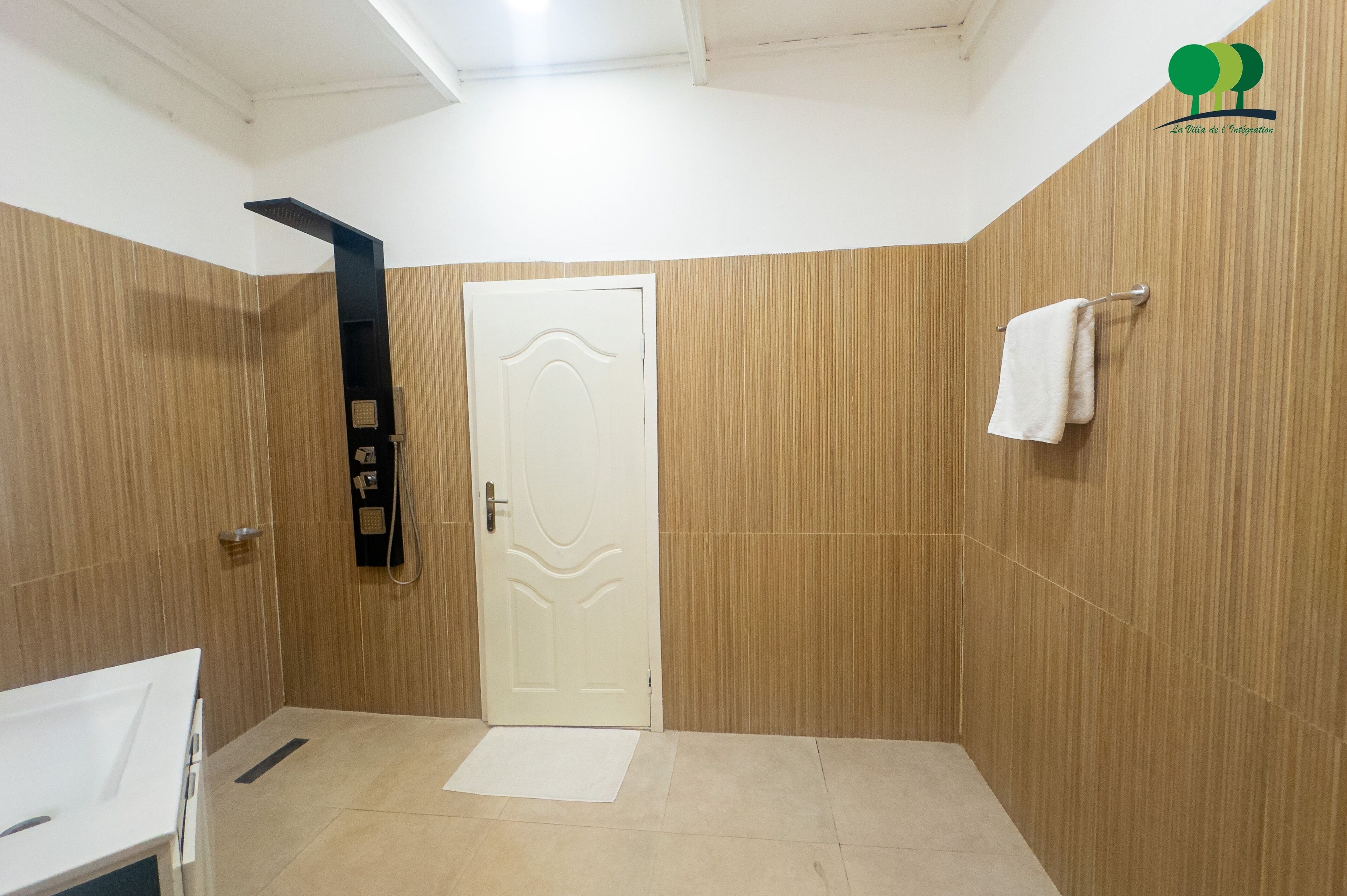 A bathroom with a white door, a towel rack, and a shower area.