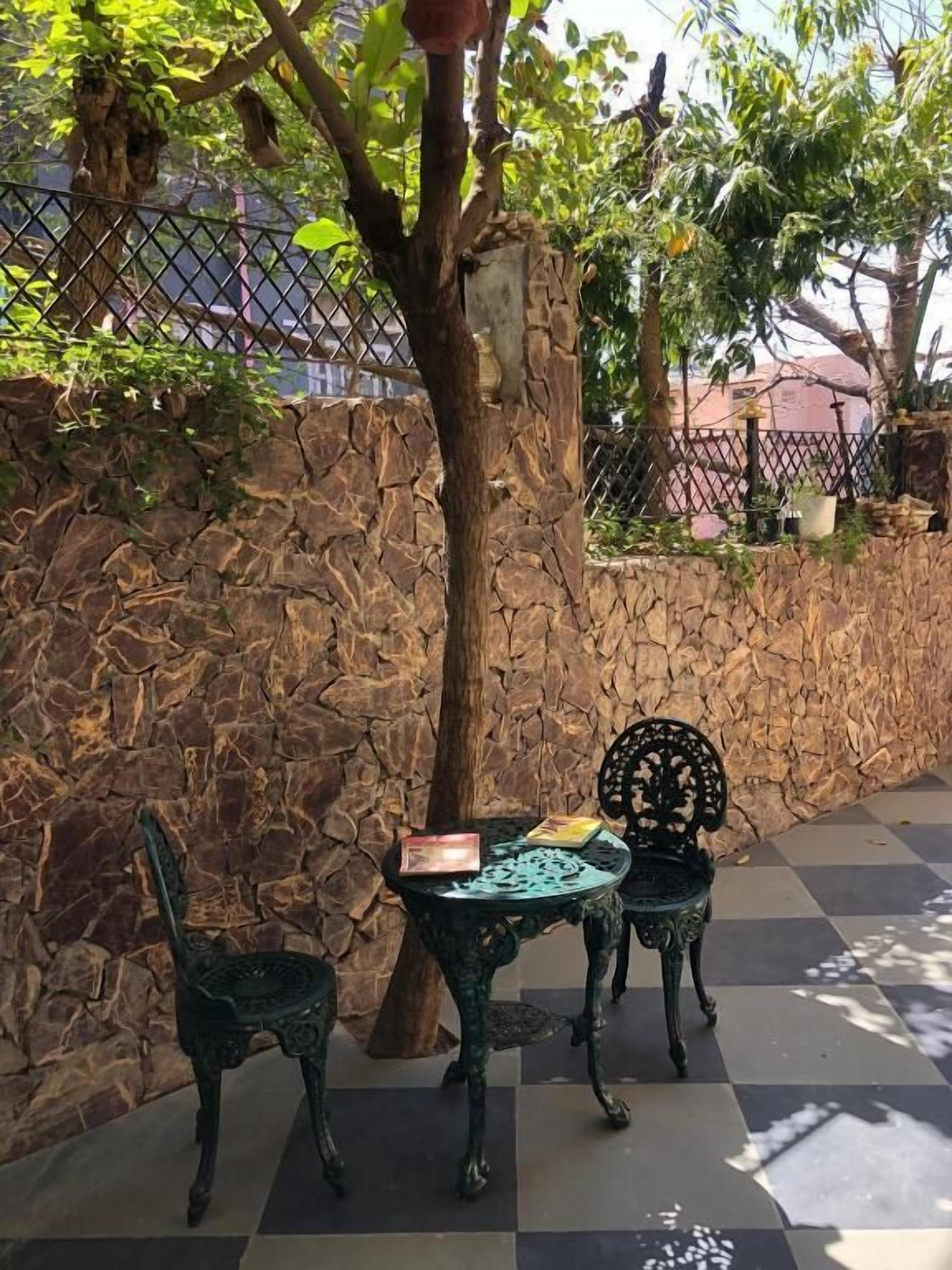 A stone wall, a tree, and two metal chairs with a book on one.