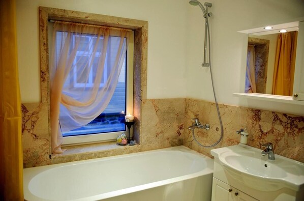 A bathroom with a bathtub, a sink, a shower, and a window with sheer curtains.