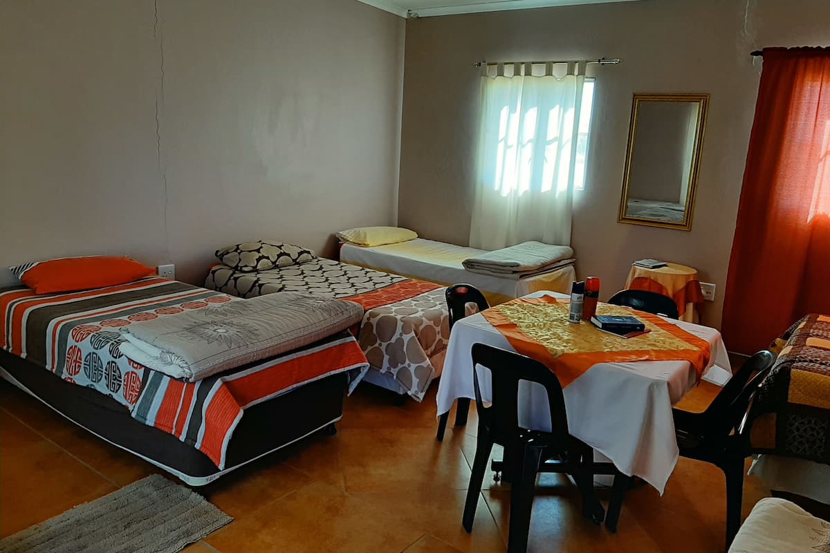A room with two beds, a table with chairs, a window with curtains, and a mirror on the wall.
