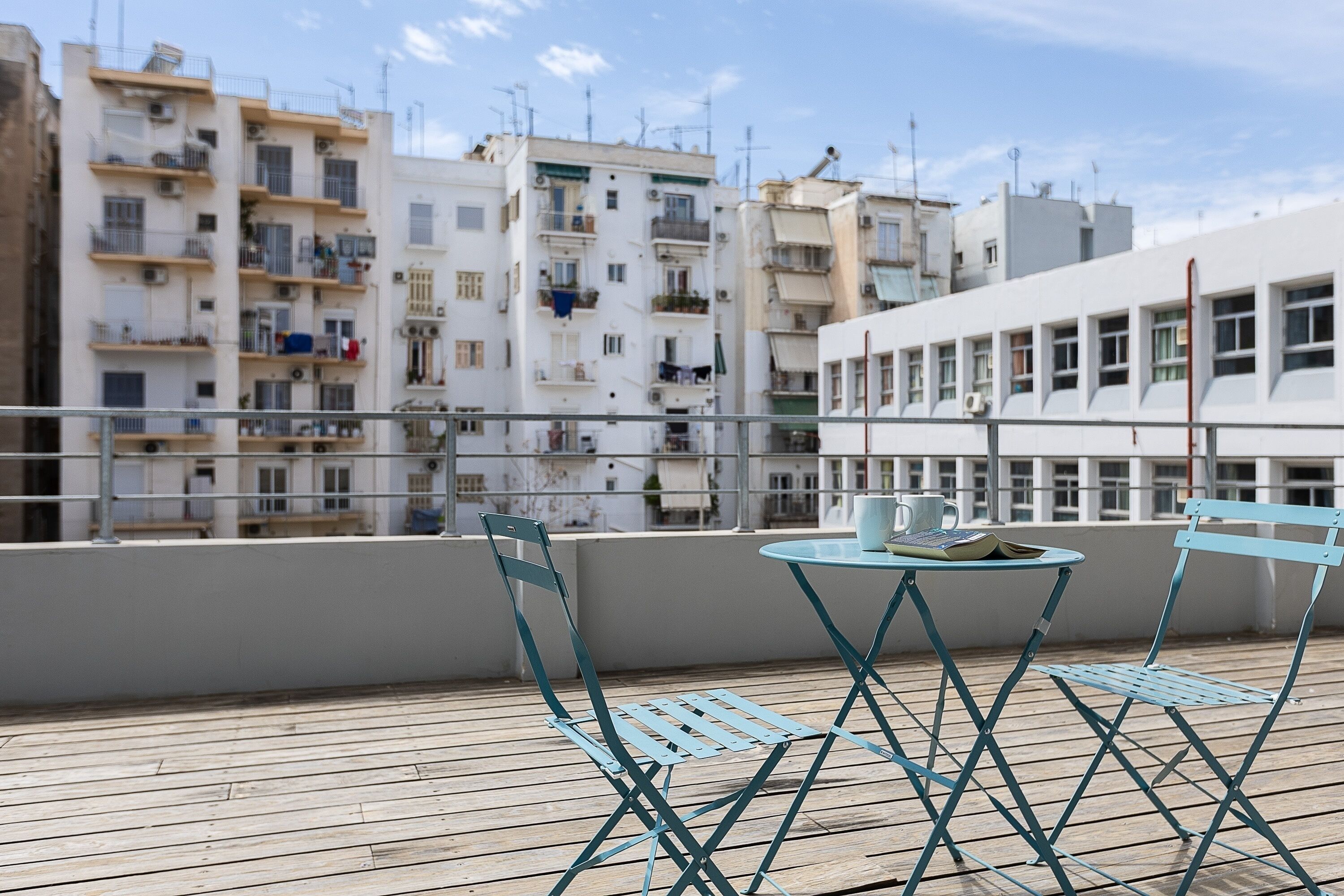 A rooftop terrace with a table and chairs, overlooking a row of residential buildings.