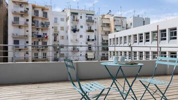 A rooftop terrace with a table and chairs, overlooking a row of residential buildings.
