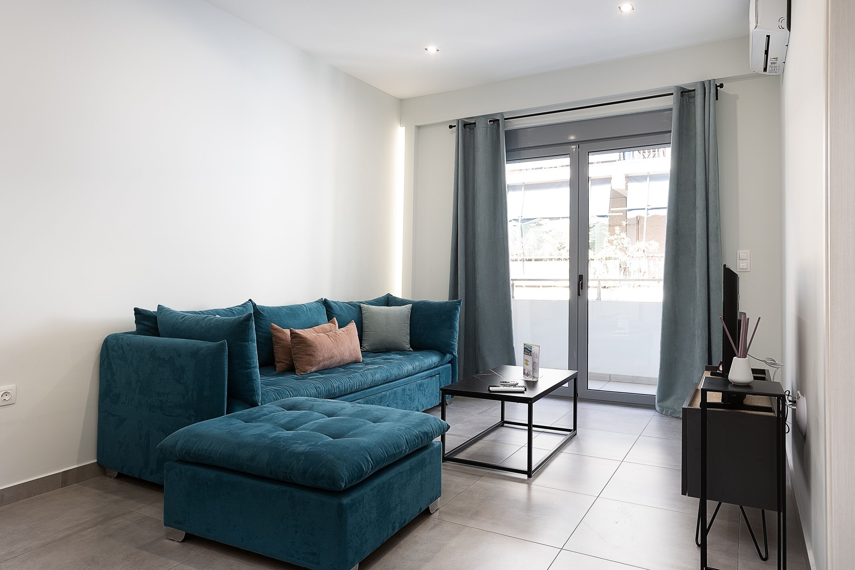 A modern living room with a teal sofa, a matching ottoman, and a small black coffee table.