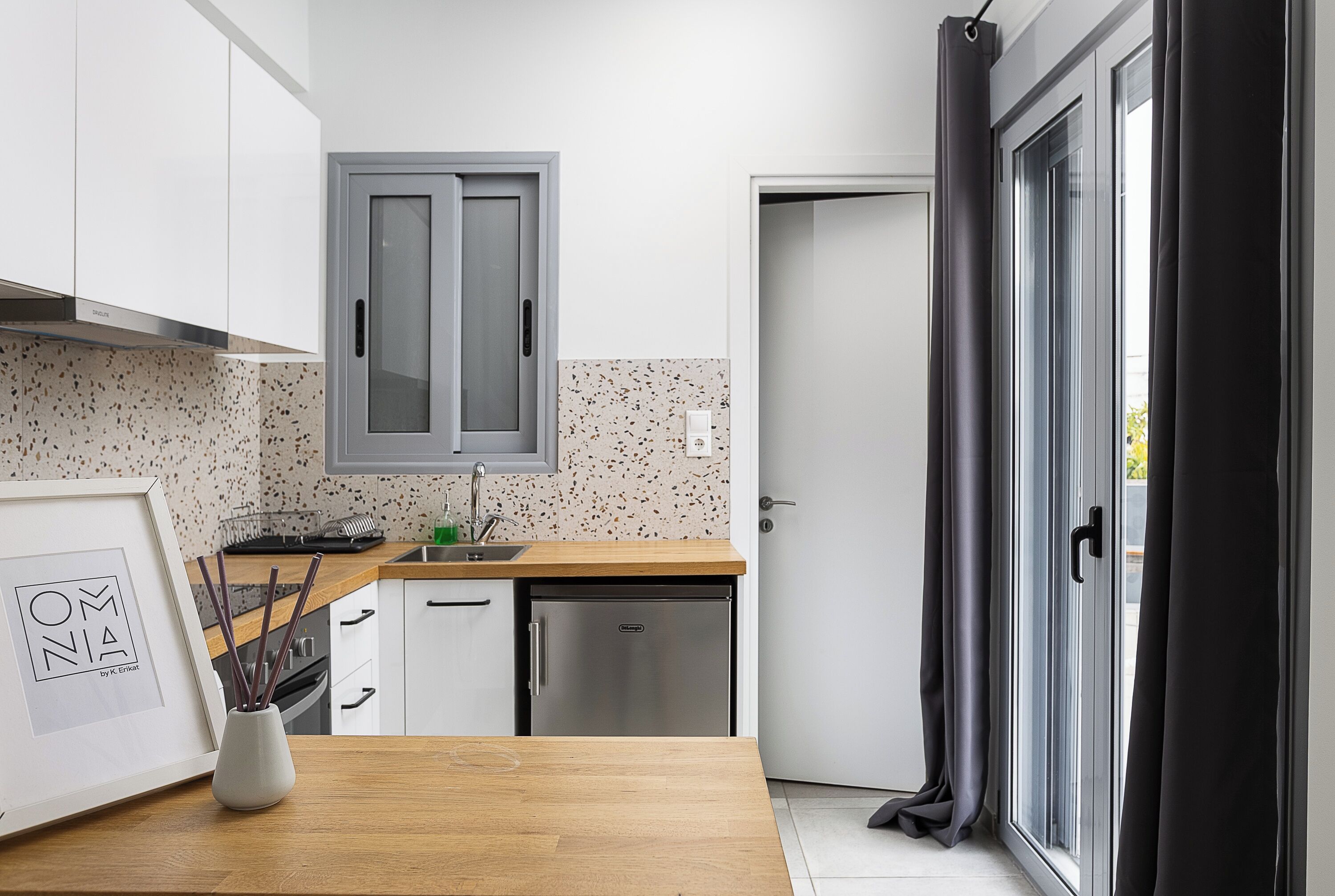 Una cocina moderna con armarios blancos, un refrigerador de acero inoxidable y una encimera de madera.
