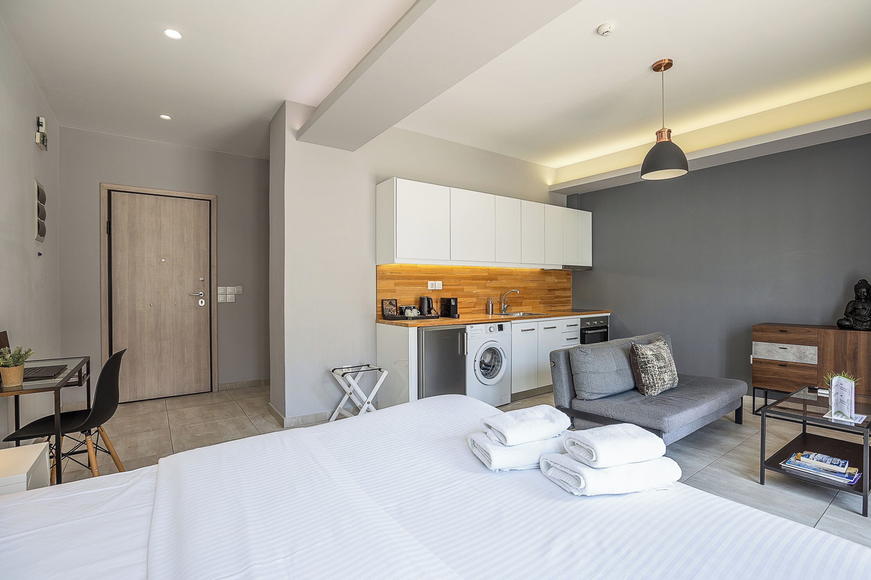 A modern hotel room with a bed, a desk, a sofa, a washing machine, and a dining area.
