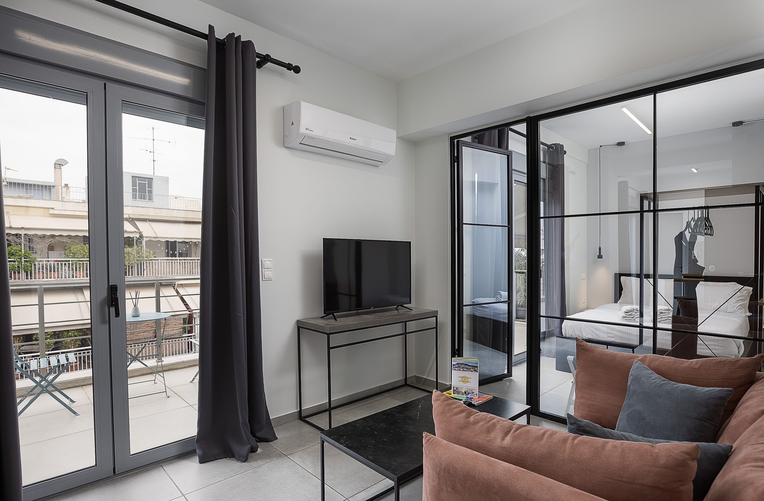 Un soggiorno moderno con una televisione a schermo piatto, un divano e una porta vetrata che dà su un balcone.
