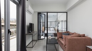 A modern living room with a sofa, a coffee table, a TV, and a sliding glass door leading to a balcony. - The Omnia Collection Pagrati (Athens)