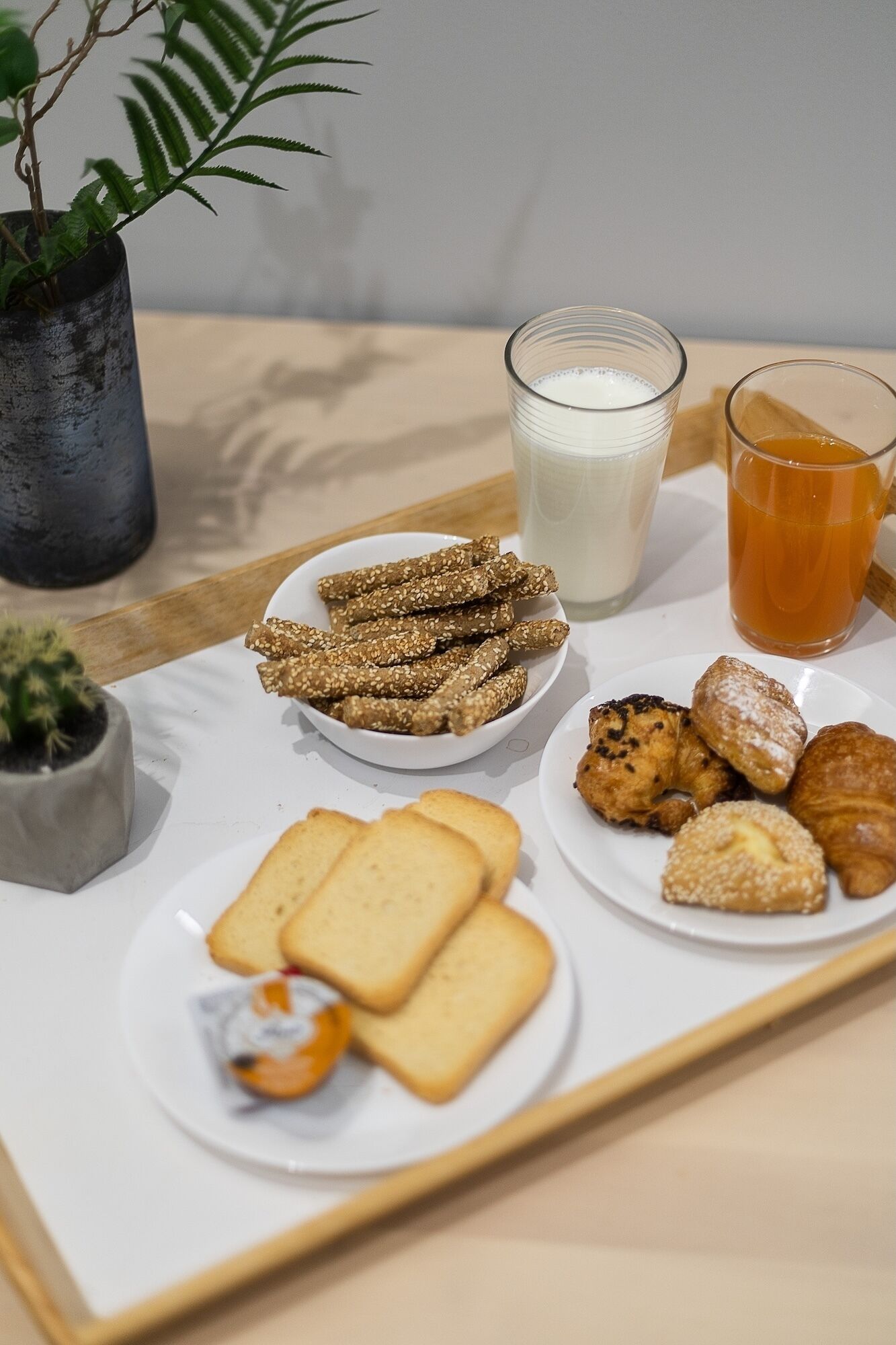 A tray with various breakfast items including toast, croissants, cookies, and a glass of milk.