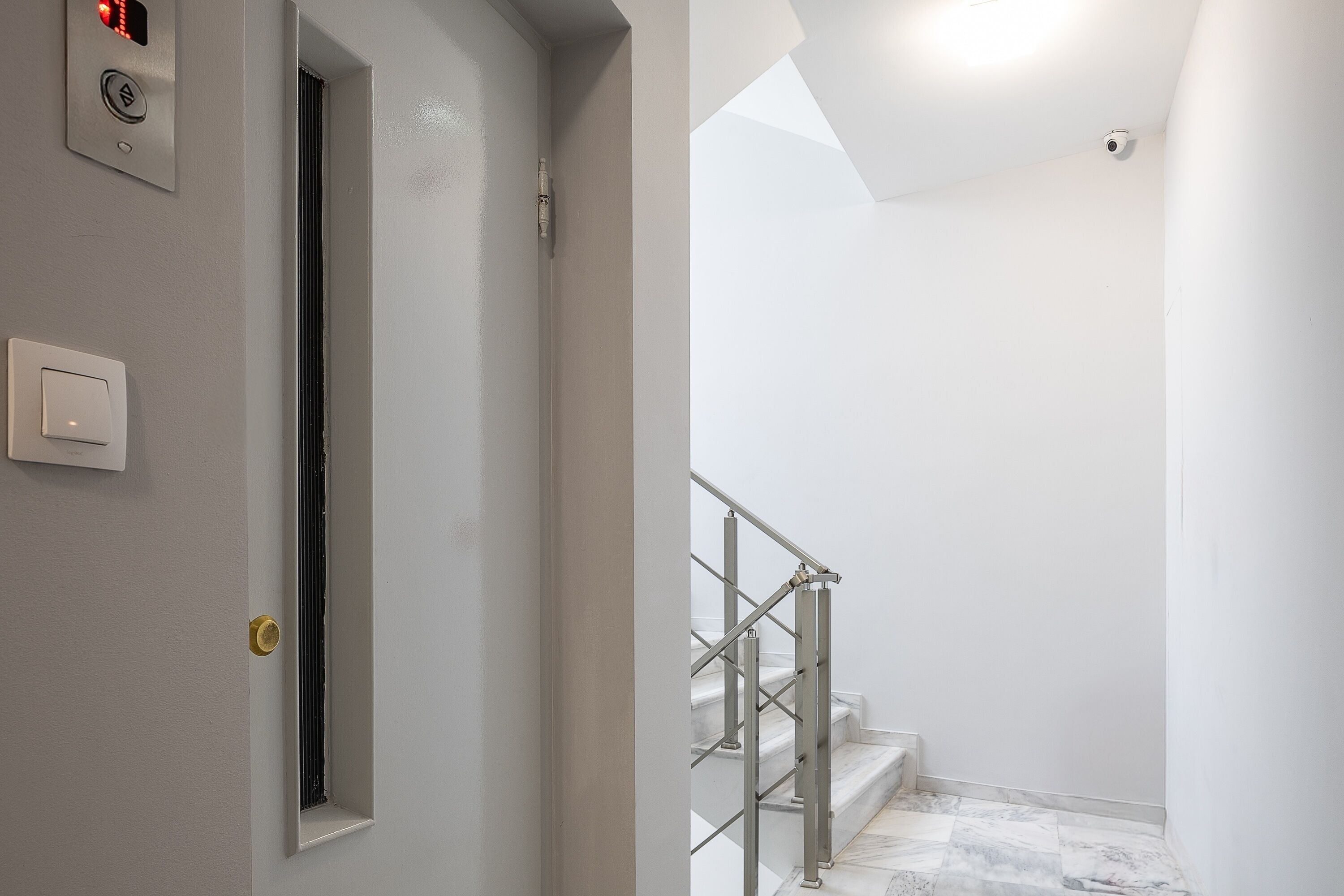 A modern interior with a door, a light switch, and a staircase with metal railings.