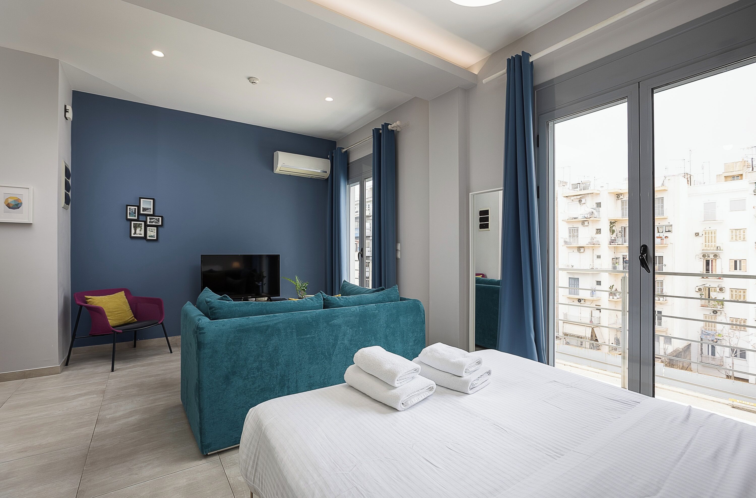 A modern hotel room with a bed, a sofa, a TV, and a large window.