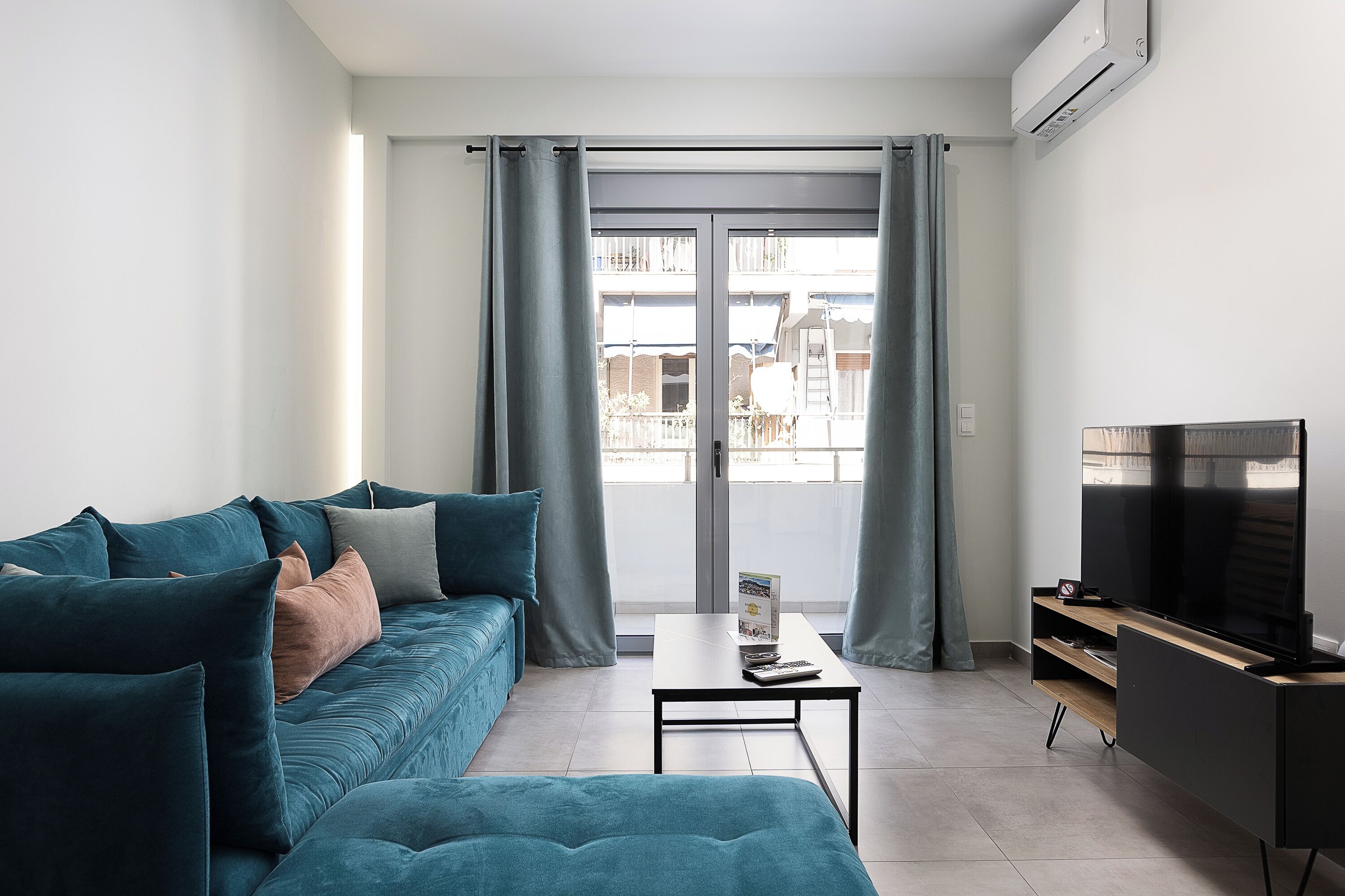 Una sala de estar moderna con sofá, mesa de centro, televisor y balcón con cortinas.