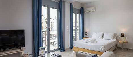 Una habitación de hotel moderna con cama, televisor, una mesa de centro de vidrio y vistas de la ciudad a través de amplias ventanas.