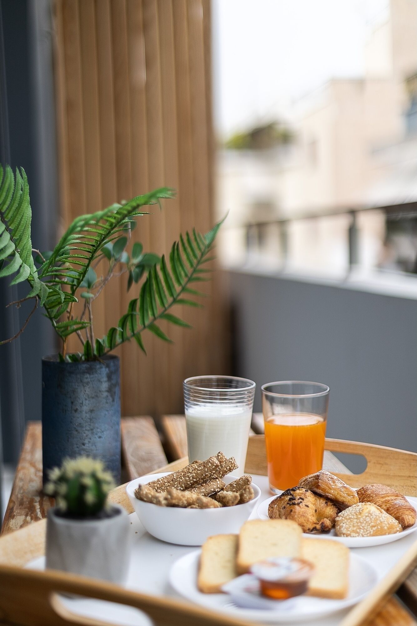 Un plateau de petit-déjeuner avec du pain, des viennoiseries et un verre de jus d’orange, posé sur une table en bois.