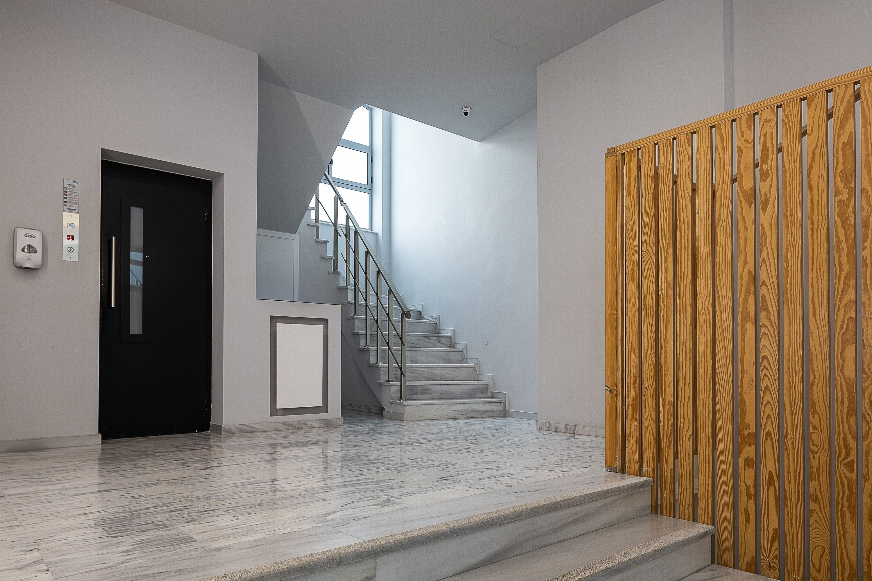 Un interno moderno con una scala in marmo, una porta nera e un pannello di legno a parete.