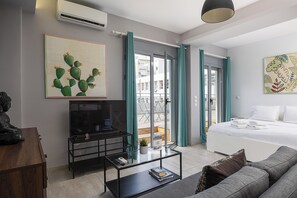 A modern hotel room with a bed, a sofa, a TV on a stand, a glass coffee table, and artwork on the walls. - The Omnia Collection Pagrati (Athens)
