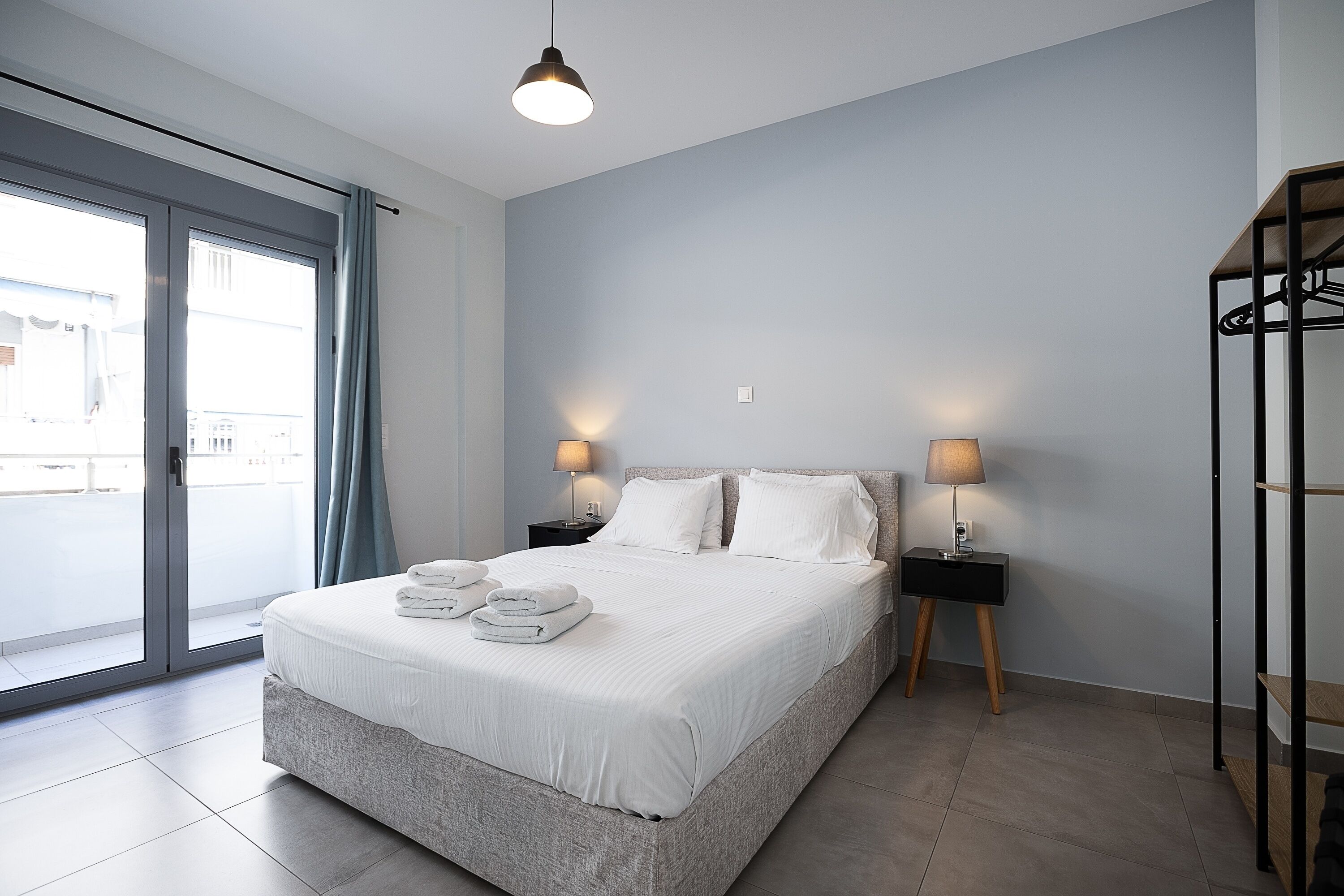 A modern bedroom with a large bed, two bedside lamps, a wardrobe, and a view through a sliding glass door.