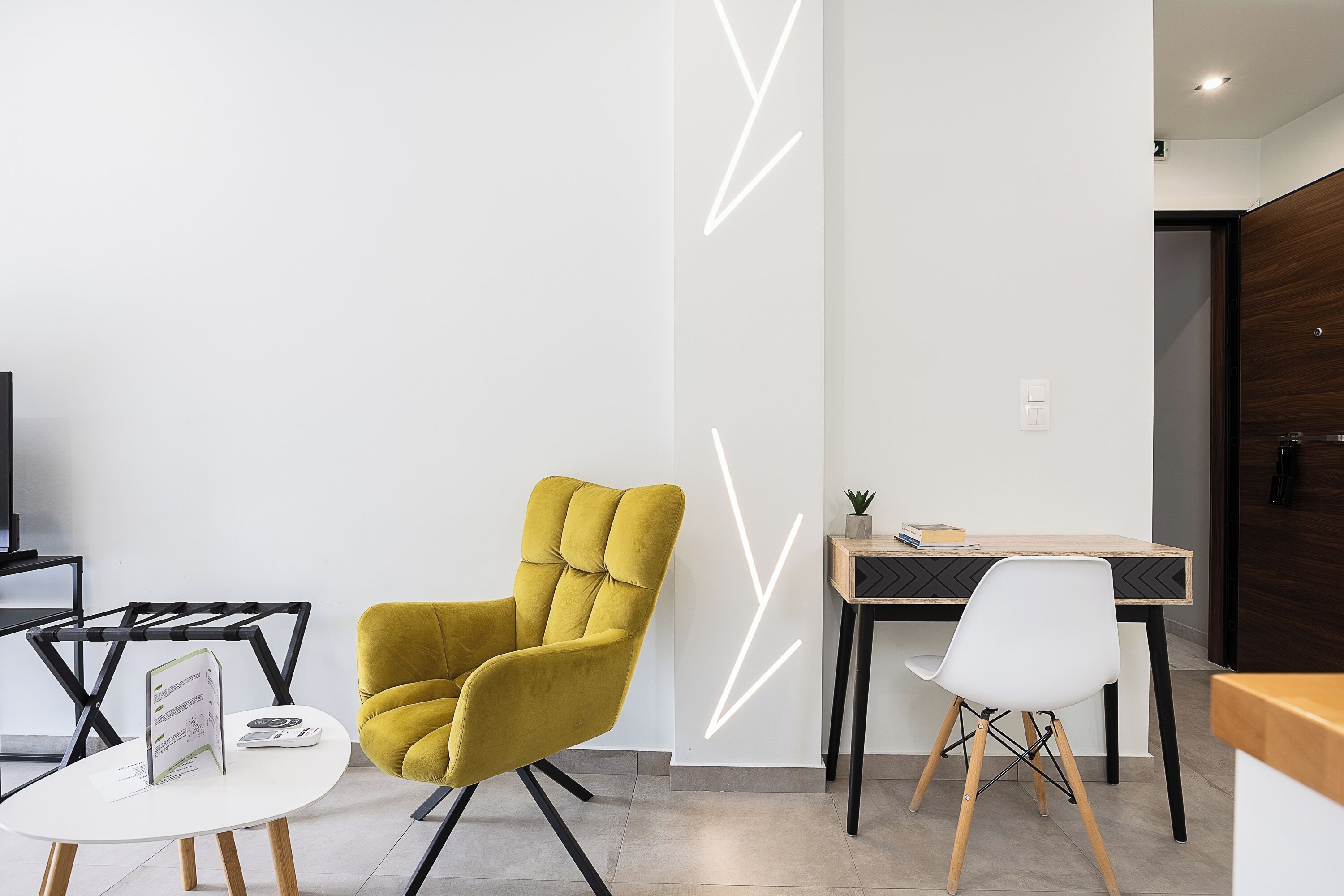 Een moderne kantoorruimte met een geel beklede stoel, een witte tafel met een bord en een bureau met een computer en een plant.