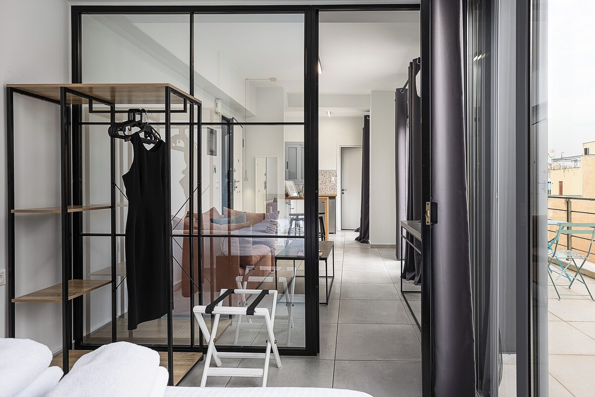 A modern interior with a glass partition, a wooden shelf unit, a white sofa, and a dining table.