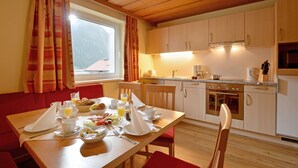 A breakfast setup with a table, chairs, and a kitchen area with cabinets and appliances. - Scheulinghof (Mayrhofen)