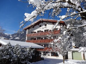 A multi-story building with balconies, surrounded by snow-covered trees and mountains. - Scheulinghof (Mayrhofen)