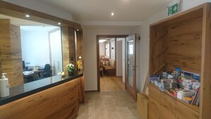 A reception area with a wooden counter, a mirror, a desk with a computer, and a magazine rack. - Scheulinghof (Mayrhofen)
