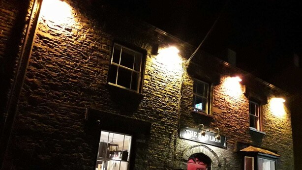 Un bâtiment en pierre sur lequel on peut lire, la nuit, une enseigne indiquant « The Red Lion ».