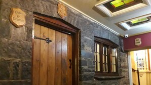 Un mur de pierre avec une porte en bois et une fenêtre. Il y a des panneaux au-dessus de la porte et de la fenêtre.