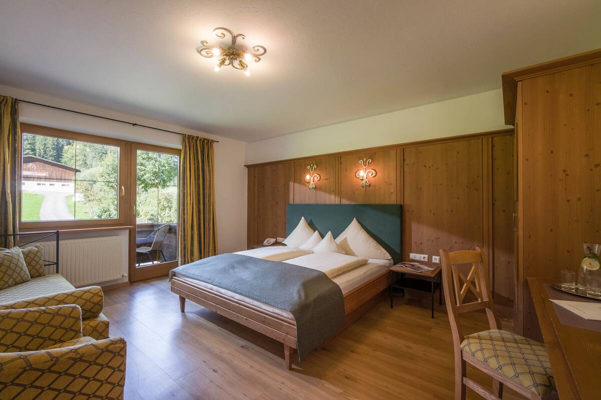 Un dormitorio con una cama grande, un cabecero de madera, un escritorio con silla y vistas al exterior a través de una ventana.