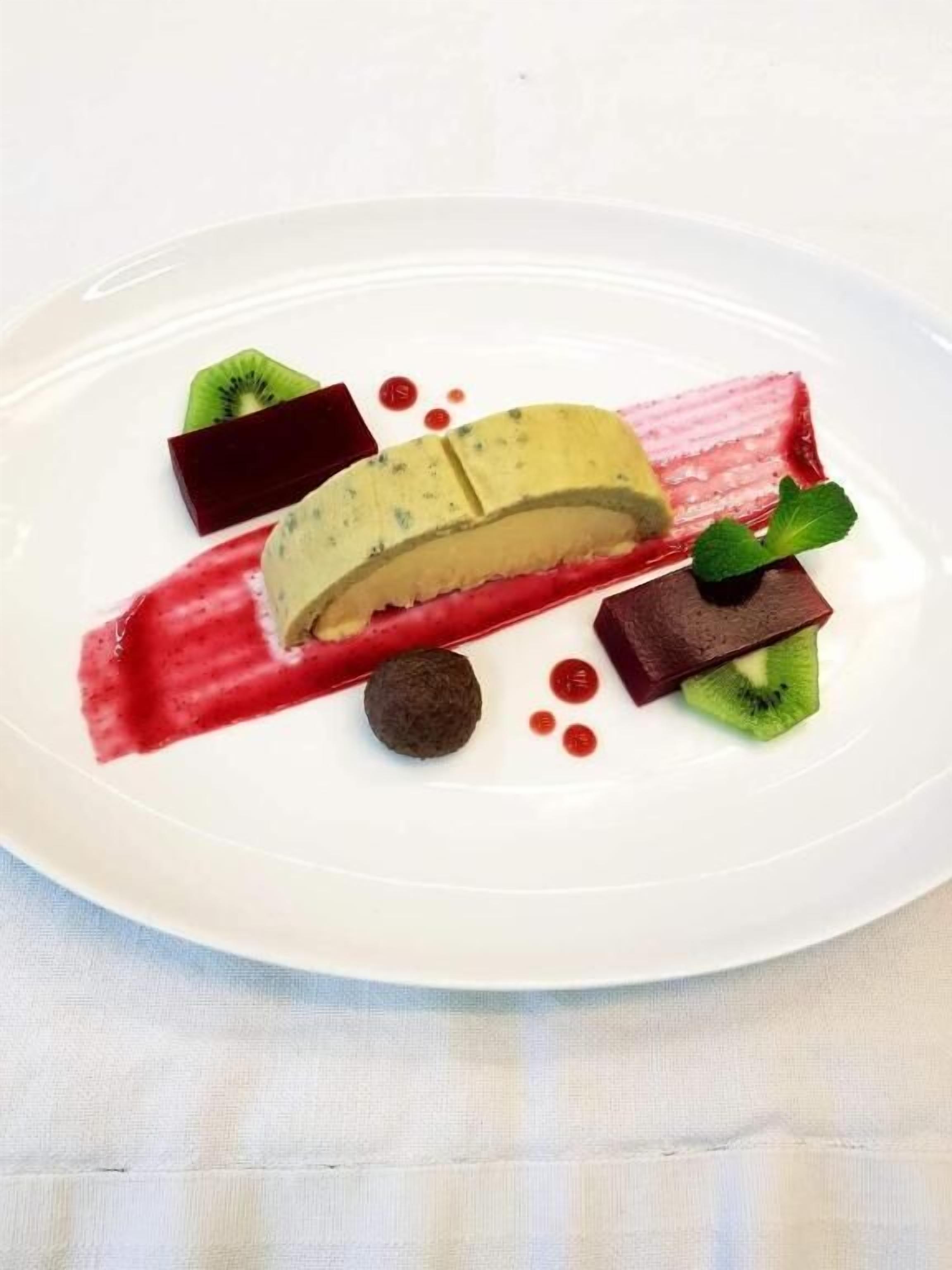 A dessert plate with a slice of cake, kiwi, and chocolate pieces.