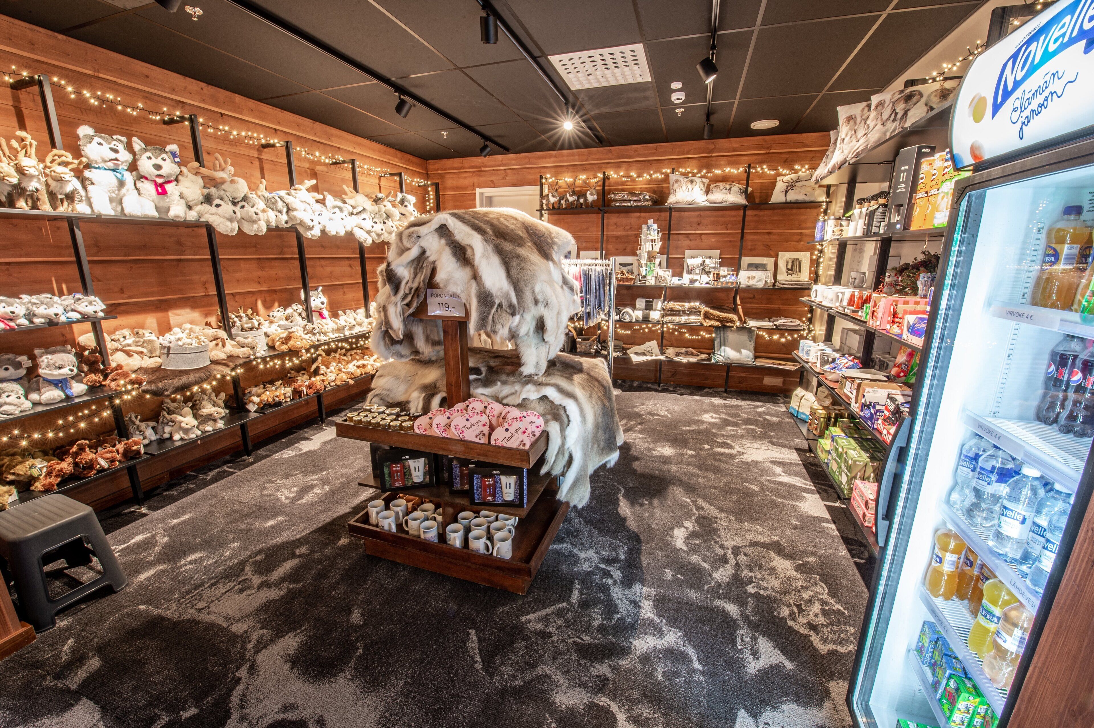 Una tienda con estantes llenos de peluches, una exhibición de tazas y una sección refrigerada con bebidas.