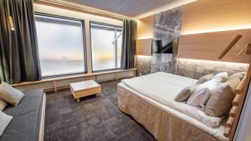 A modern hotel room with a large bed, a bench, and a view through a large window.