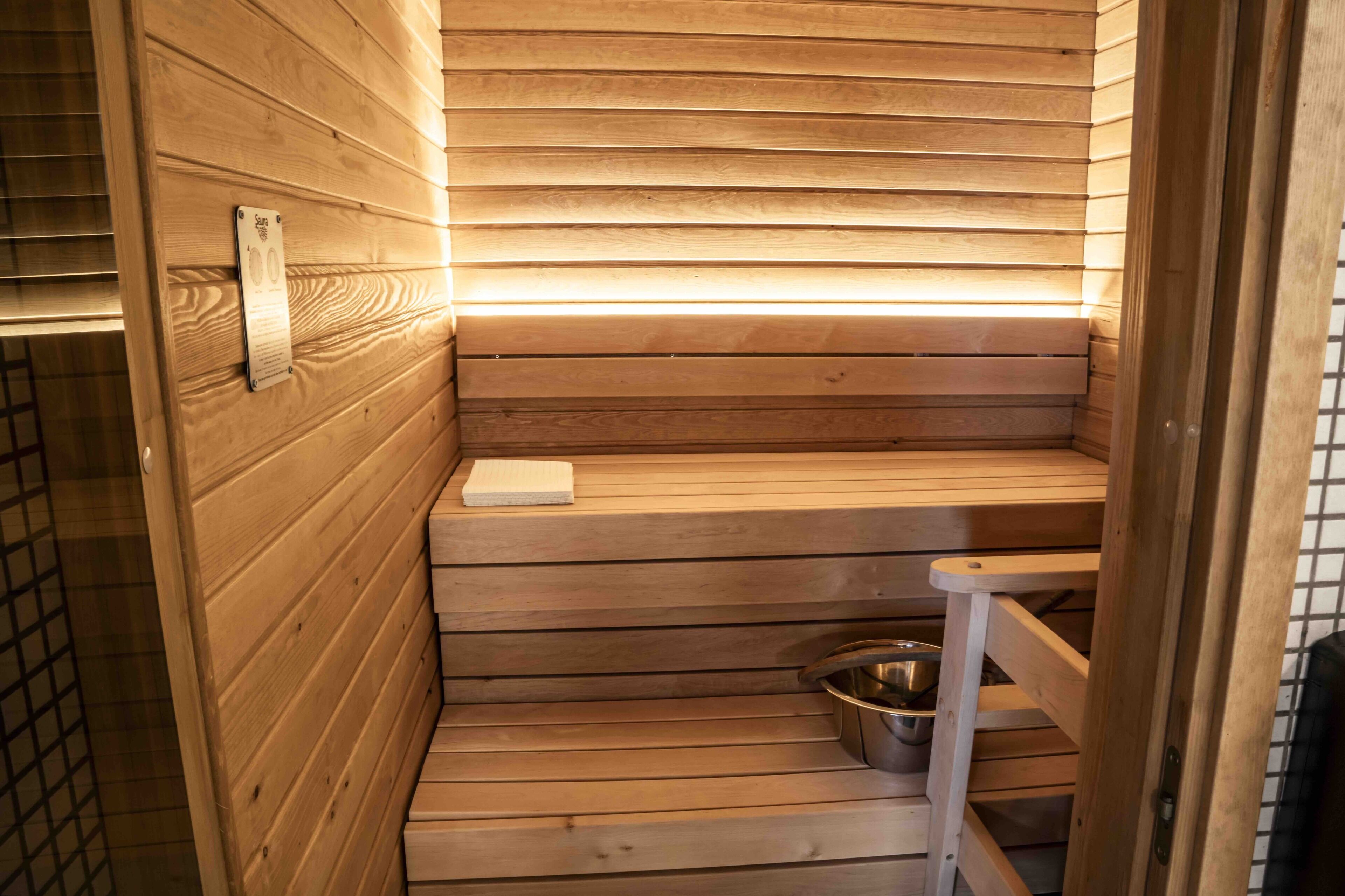 Uma sauna de madeira com um banco e uma bacia de metal.