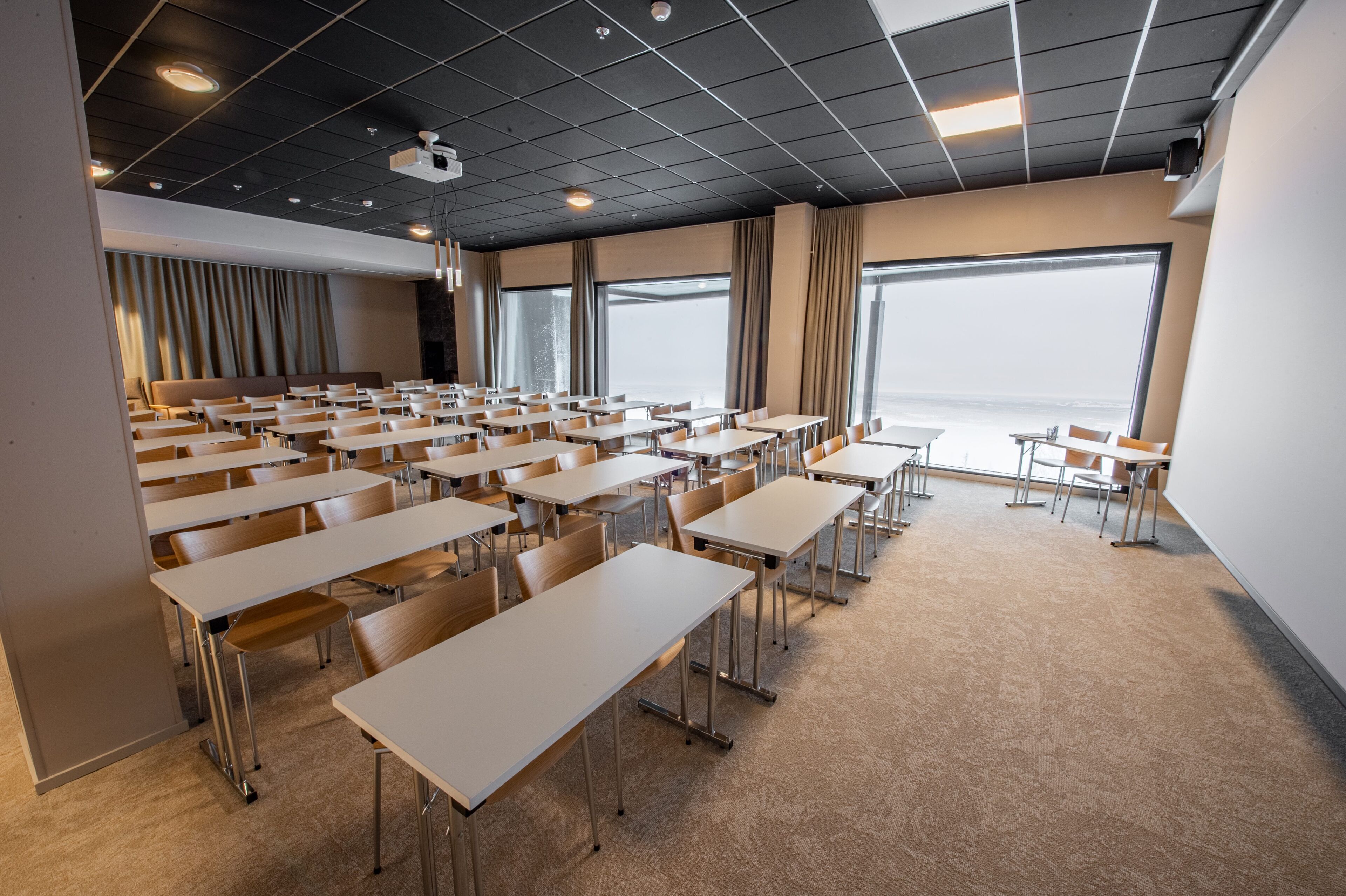 A conference room with rows of tables and chairs, large windows, and a modern ceiling design.