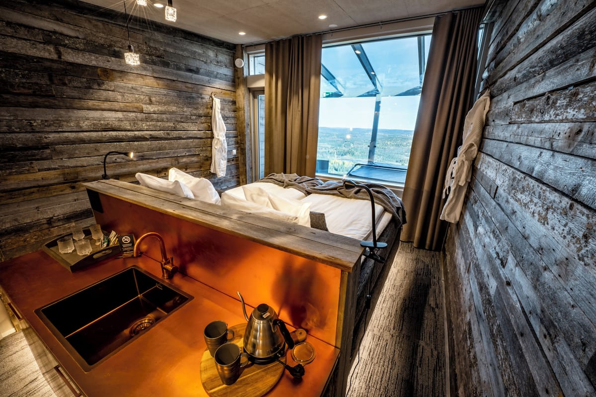 Una habitación tipo cabaña con interior de madera, una cama, un lavamanos con hervidor y un ventanal con vistas.