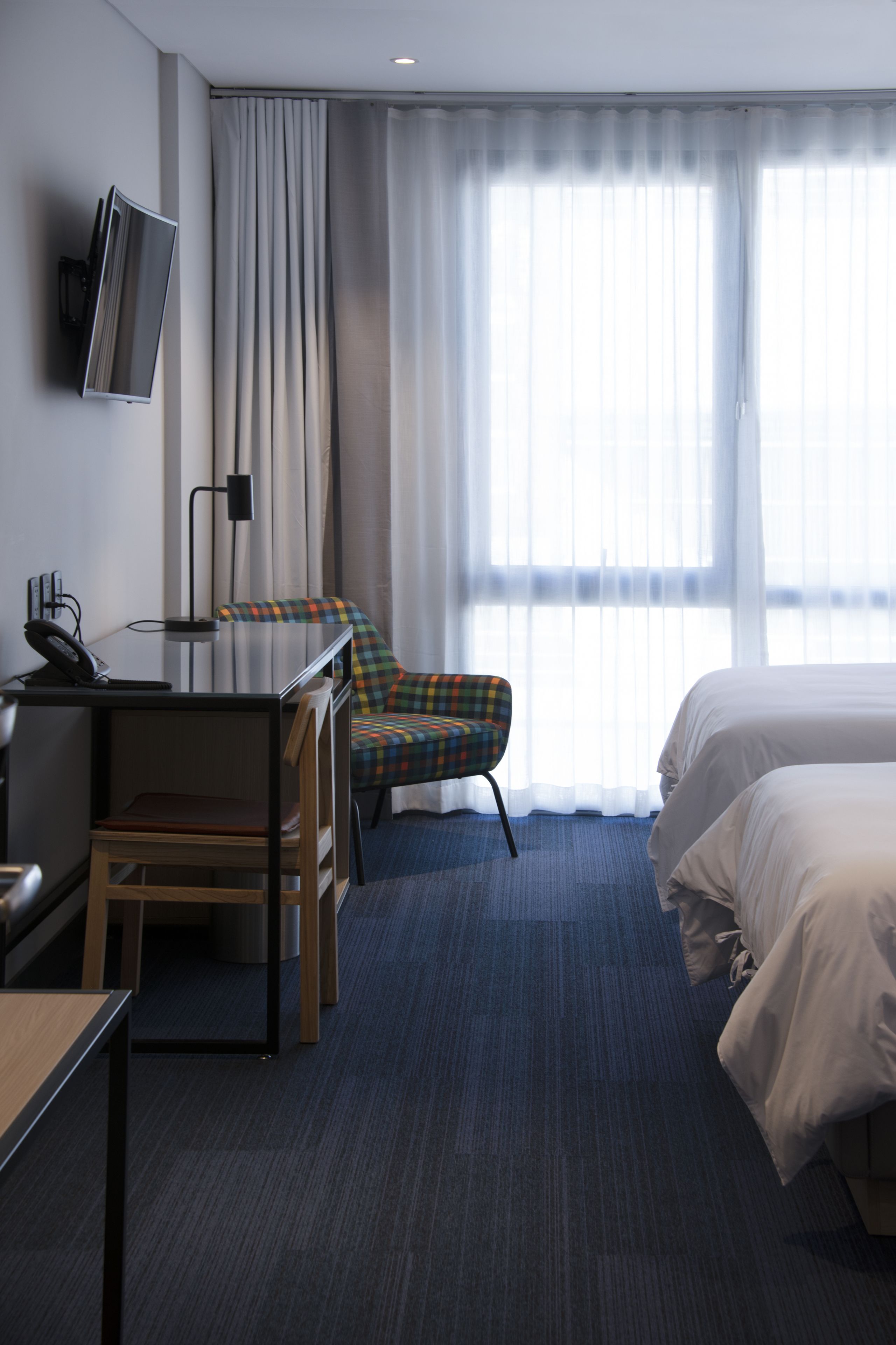 Una camera d'albergo con scrivania, sedia, letto e televisore fissato al muro.
