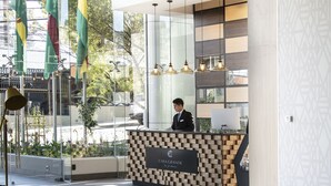 A modern hotel lobby with a reception desk, seating areas, and large windows offering a view of the outdoors.