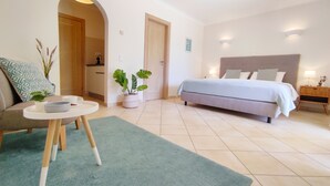 Une chambre à coucher comprenant un lit, des tables de chevet, une petite table avec un bol et une tasse, une plante en pot et une porte donnant sur une autre pièce.