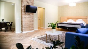 Una habitació d'hotel amb una paret d'accent de maó, una televisió de pantalla plana, un llit amb roba de llit blanca, un sofà blau, una taula rodona petita i una planta en test.