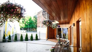 Un edifici de fusta amb terrassa coberta, seients a l'aire lliure i cistells florals penjants.