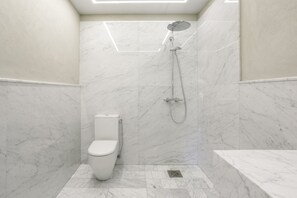 A modern bathroom with a toilet, shower, and marble walls.