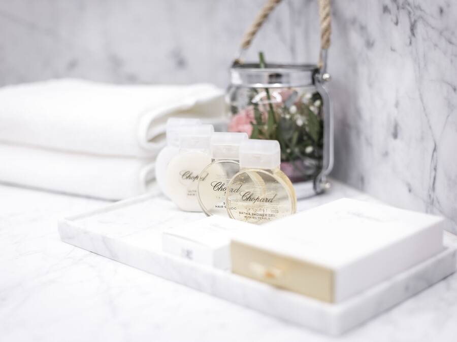 A bathroom vanity with a marble countertop, a white towel, and three bottles of 'Chopard' bath products.