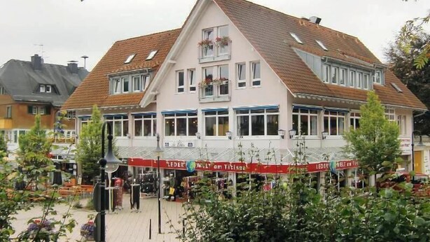 A two-story building with a sloped roof, large windows, and a sign reading "LEDERWELT am Thiem". - Appartementhaus Am Roten Platz (Titisee-Neustadt)