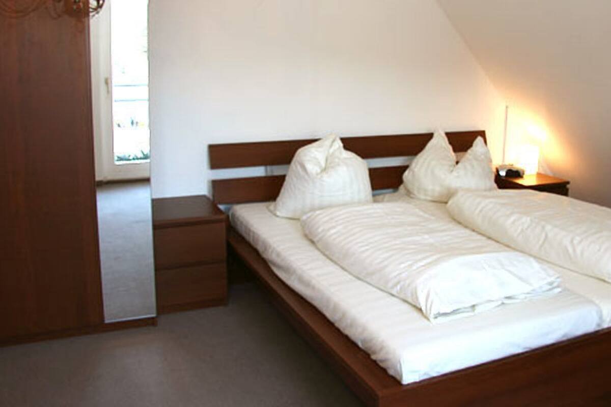 A bedroom with a double bed, a nightstand, and a wooden wardrobe.
